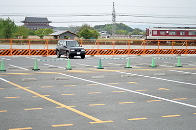 撤去される平城宮跡内の県仮設駐車場。工事用の柵の向こうではすでにアスファルトがはがされ、白っぽい地面が現れている。奥は大極殿＝2016年4月25日、奈良市佐紀町