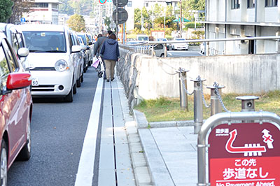 前方の県庁西交差点の信号待ちで連なる車すれすれに歩く人たち＝2016年11月6日午後3時17分ごろ