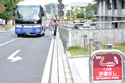 歩行者をよけるバス。バスターミナルが完成して、車体の大きな観光バスの通行が増えると車道歩行の危険性は高まるとみられる。右端の建物は県庁議会棟＝2016年10月23日午前9時21分ごろ、奈良市登大路町