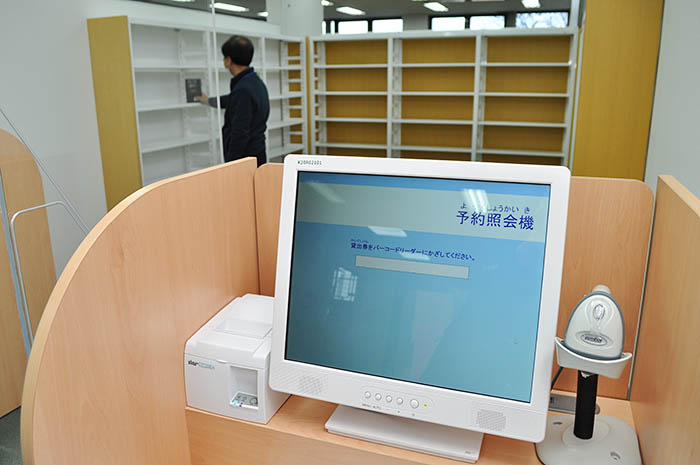 奈良市立西部図書館予約図書受け取りコーナー。利用者は手前の予約照会機で取り置き番号を印字したレシートを受け取り、番号に従って奥の書棚から予約した本を取り出す＝2020年12月22日、同市鶴舞西町