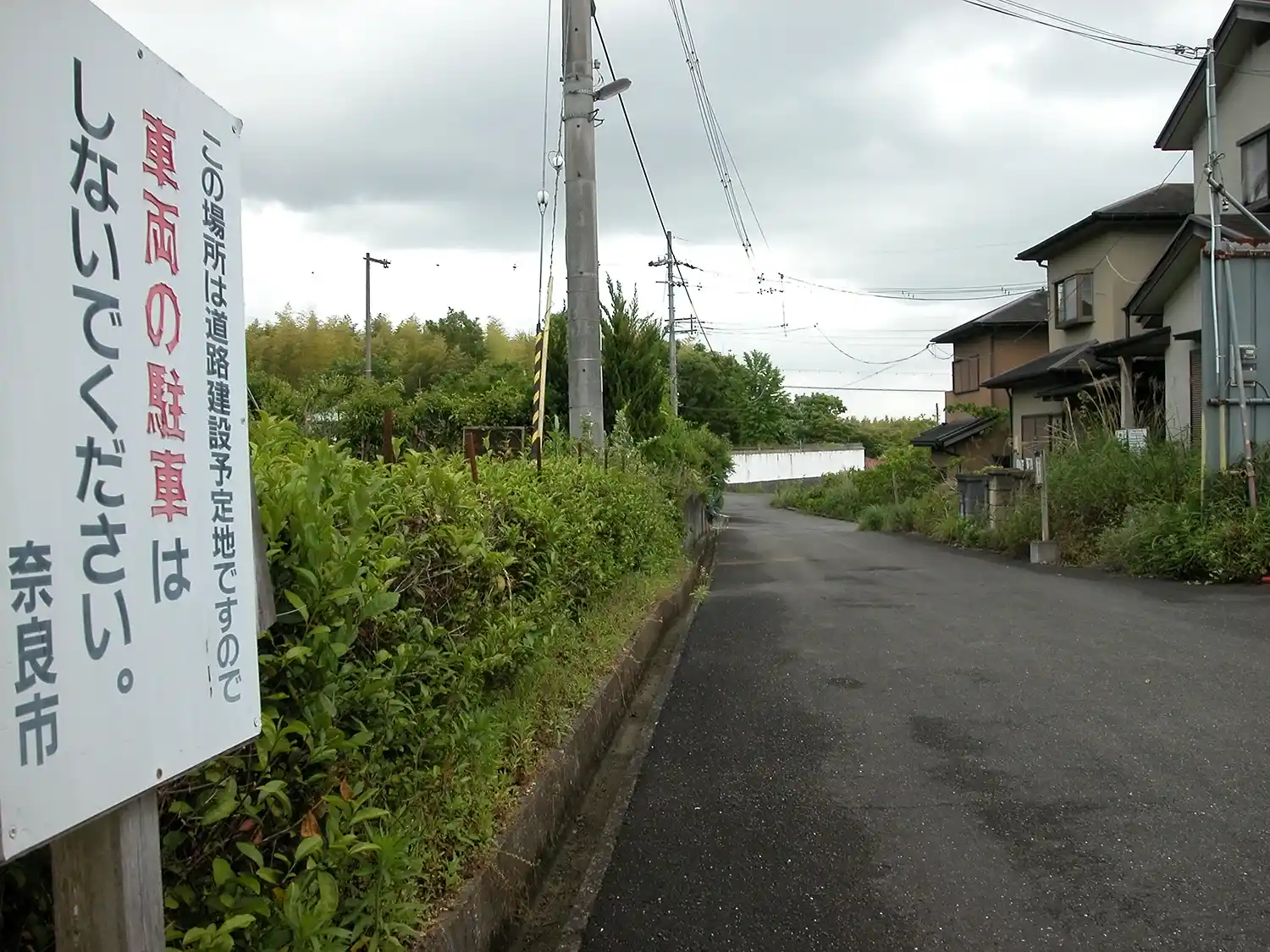 舗装された塩漬け土地の古市光ケ丘線用地と3棟の違法な建売住宅（右）＝2023年5月23日、奈良市古市町