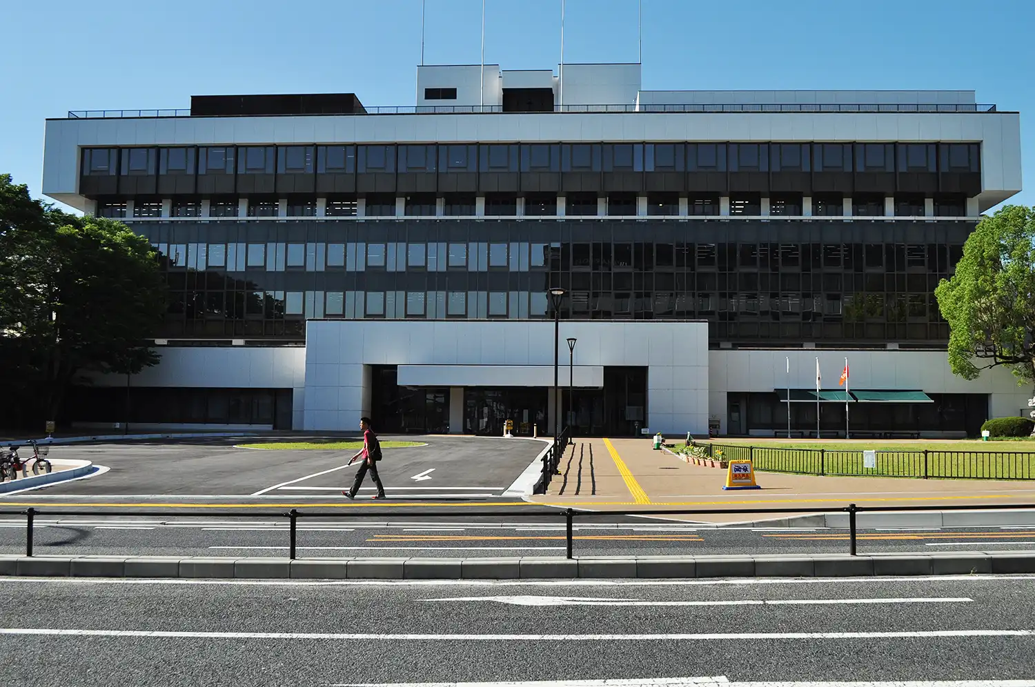 通りから望む奈良市役所の正面。入り口に市役所の表示がない。右は整備された芝生広場＝2024年7月5日、同市二条大路南1丁目