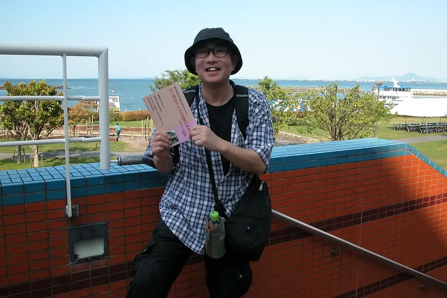 仲間たちとレクリエーション活動を楽しんだ琵琶湖を背に刊行した著書を手にする江端一起さん＝2024年9月6日、滋賀県大津市内