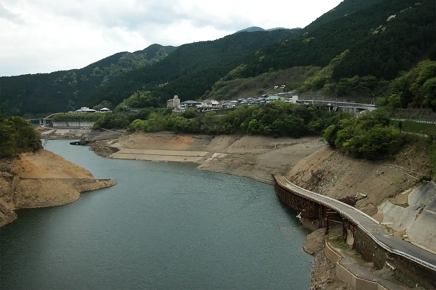 上の写真と同じ位置から写した現在の大滝ダム貯水池。水位が下がり水没したダム建設工事用の土砂運搬道（右下）が姿を現した＝2026年4月22日、浅野詠子撮影